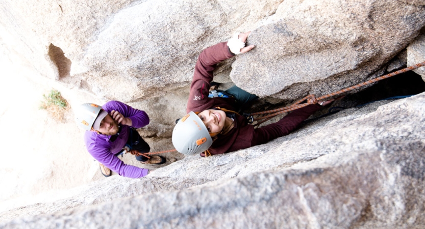 Two people wearing safety gear are attached to ropes as they navigate a narrow canyon. 